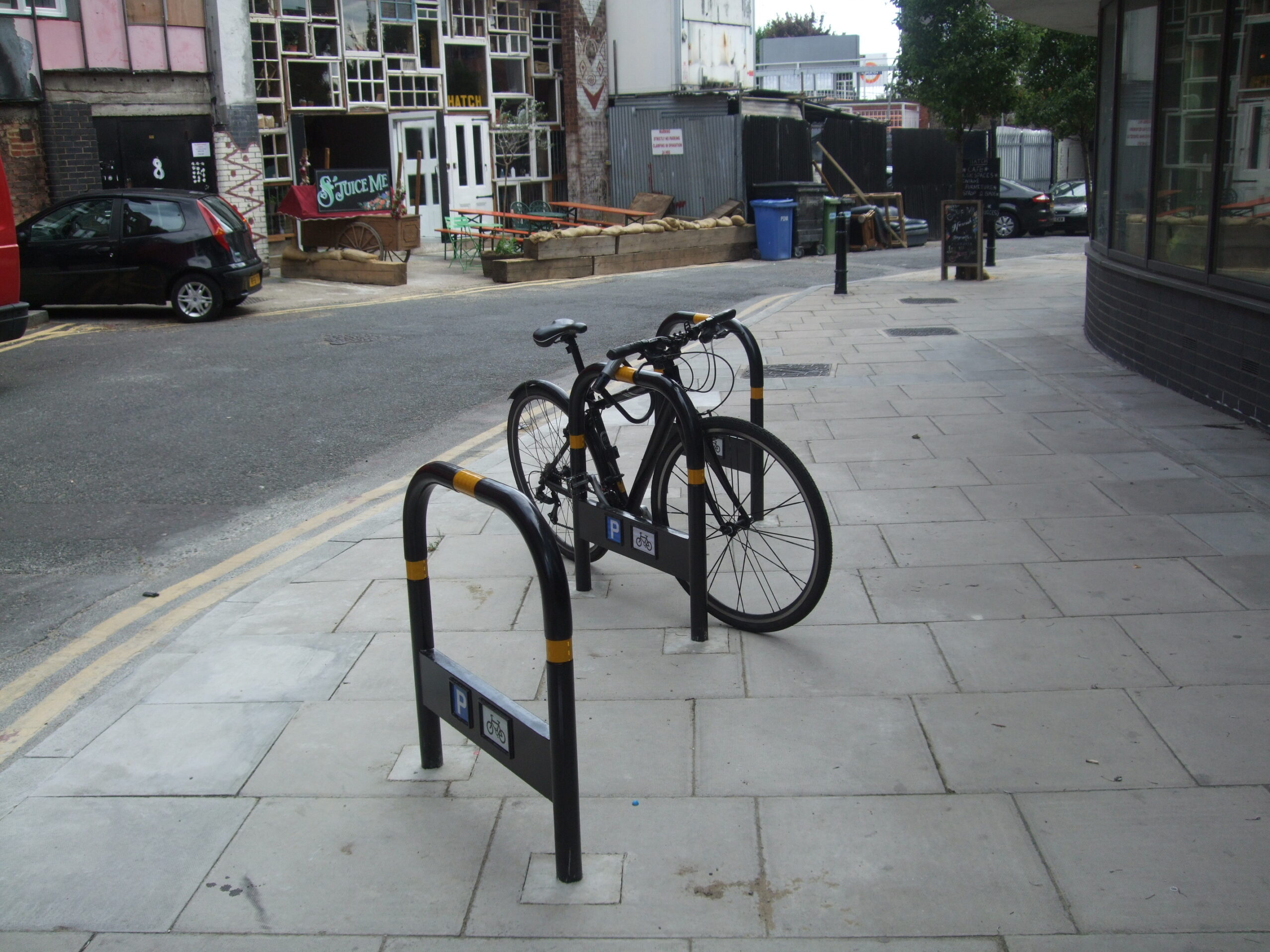 A black bicycle parked securely on a metal cycle stand, located on a footway.